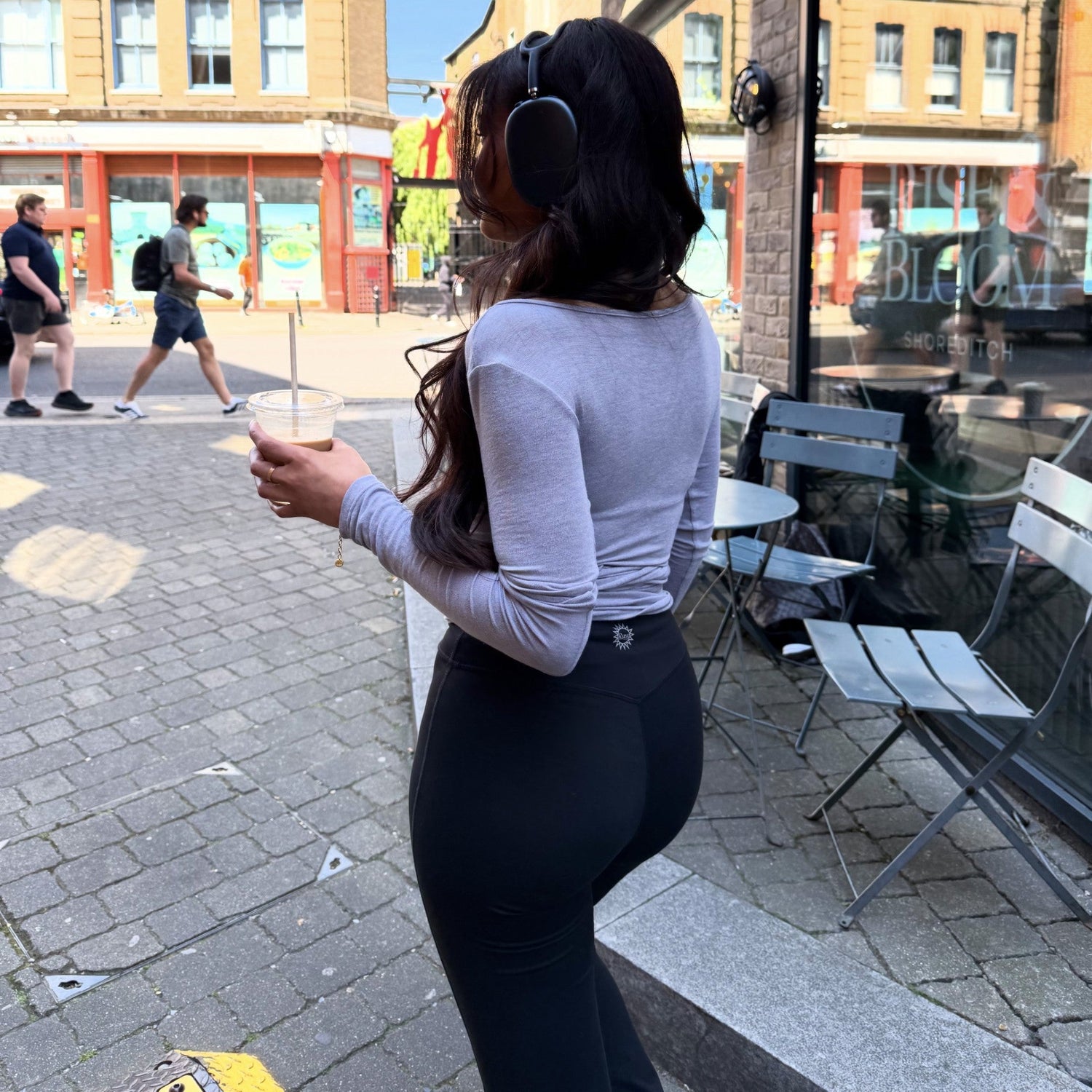 A woman wearing Ruay Muse Reformer Wrap Top with leggings while grabbing a coffee to go and wearing headphones