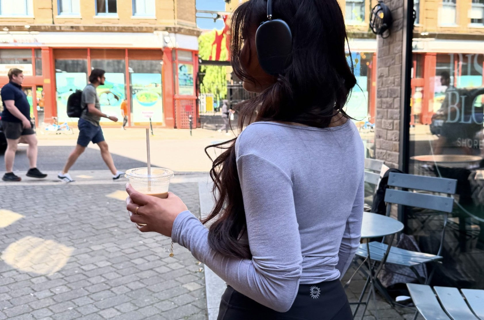 Woman wearing Ruay Muse Wrap top and leggings, wearing headphones and holding a drink on a city street
