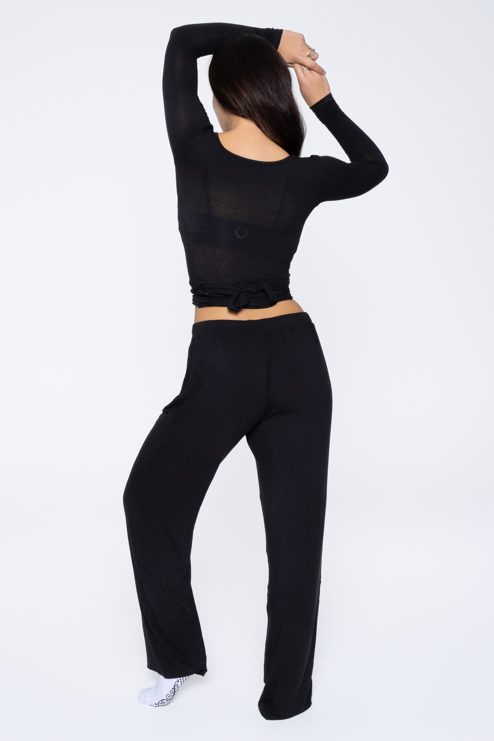 Back shot of model wearing Ruay Muse Reformer wrap top and trousers in black